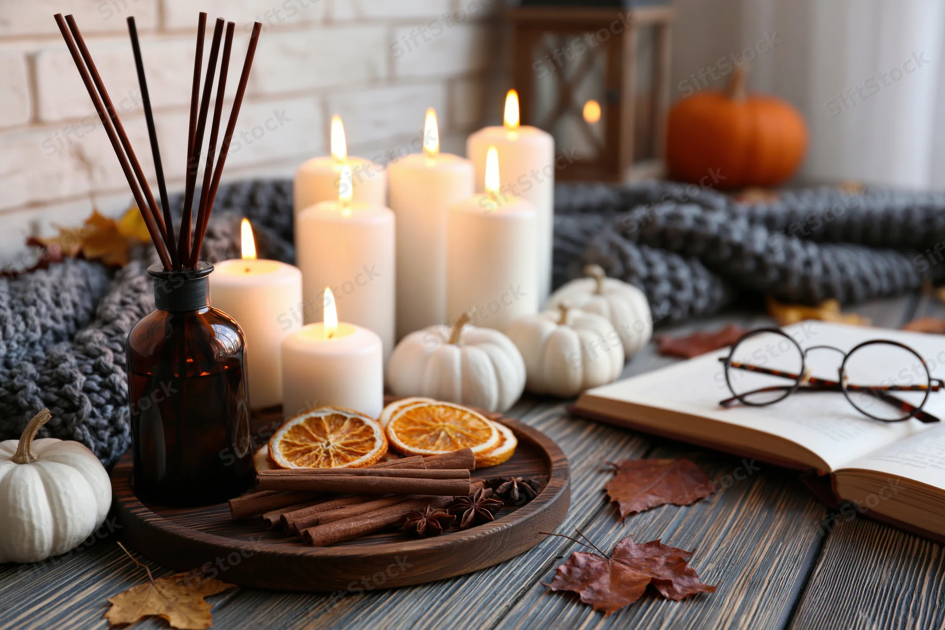 Autumn still life with lit candles, pumpkins, book and glasses on rustic wooden table