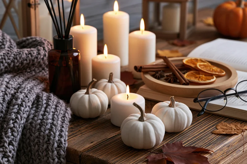 Still life with lit candles, white pumpkins, and autumn decor on a rustic wooden table