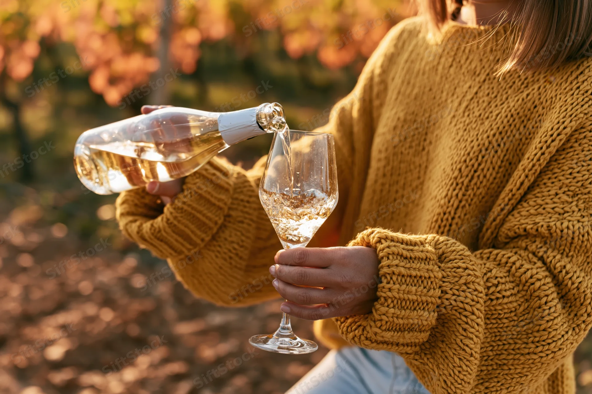 Woman pouring white wine from a bottle into a glass in a vineyard at sunset