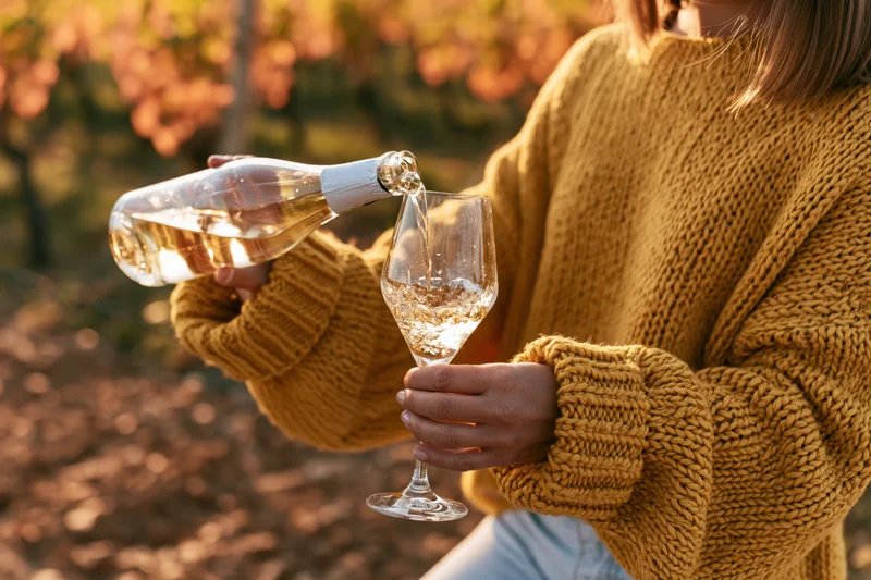 Woman pouring white wine from a bottle into a glass in a vineyard at sunset