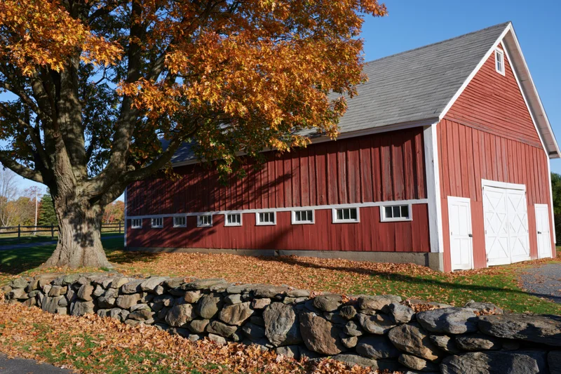 Red barn with white trim and autumn foliage beside a stone wall in rural landscape