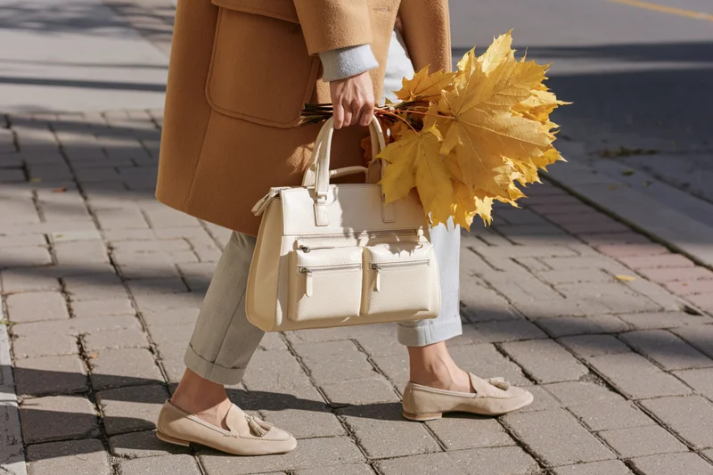 Woman walking on a brick sidewalk carrying a handbag and yellow maple leaves in autumn