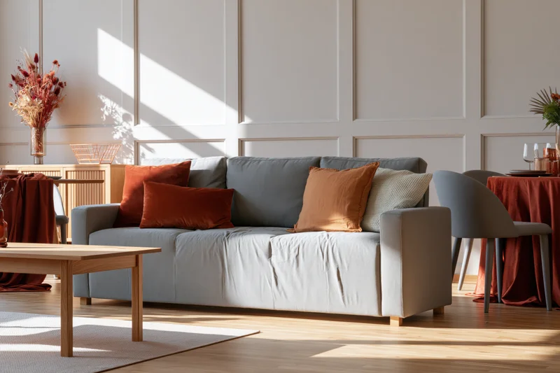 Gray sofa with orange and brown cushions in a bright modern living room with wooden flooring and sunlight streaming through windows