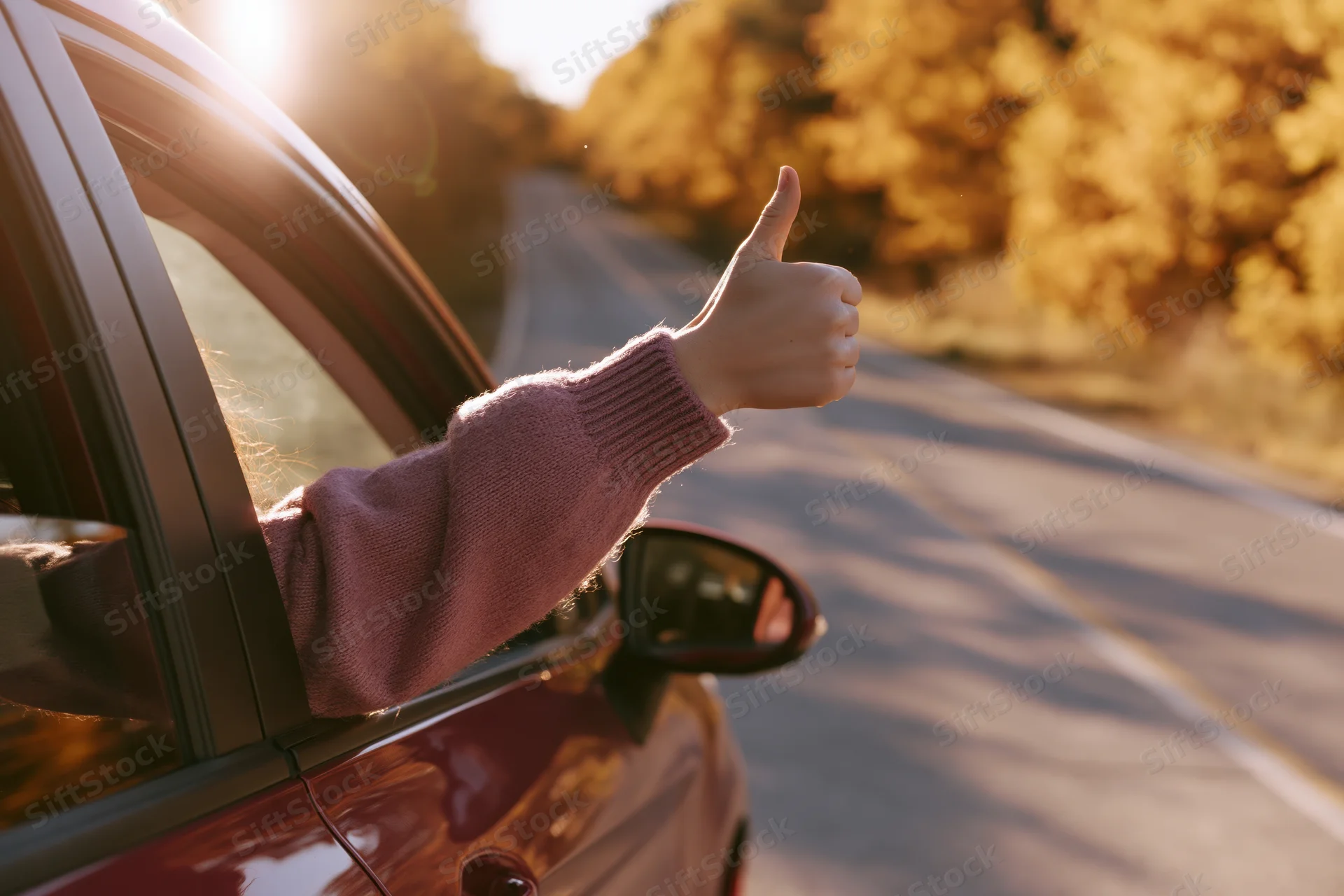 Woman’s arm out of car window giving thumbs up on autumn road