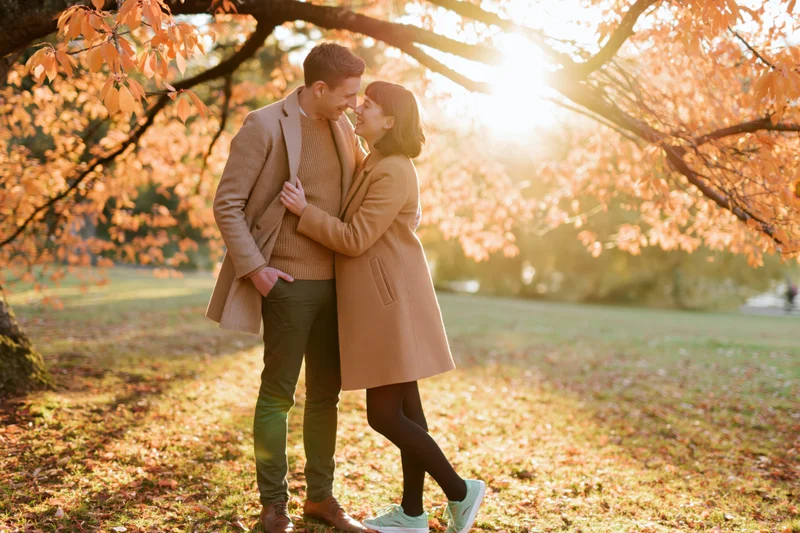 Couple embracing under autumn tree in park with sunlight filtering through leaves