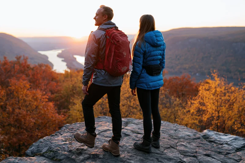 Couple standing on rocky outcrop overlooking autumn valley at sunset