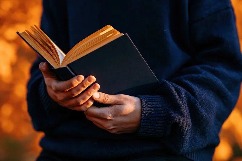 Person reading an open book outdoors in autumn foliage