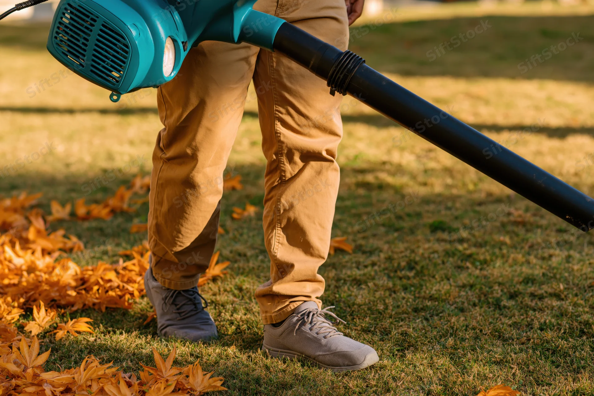 Man using leafblower to clear fallen leaves on a grassy yard