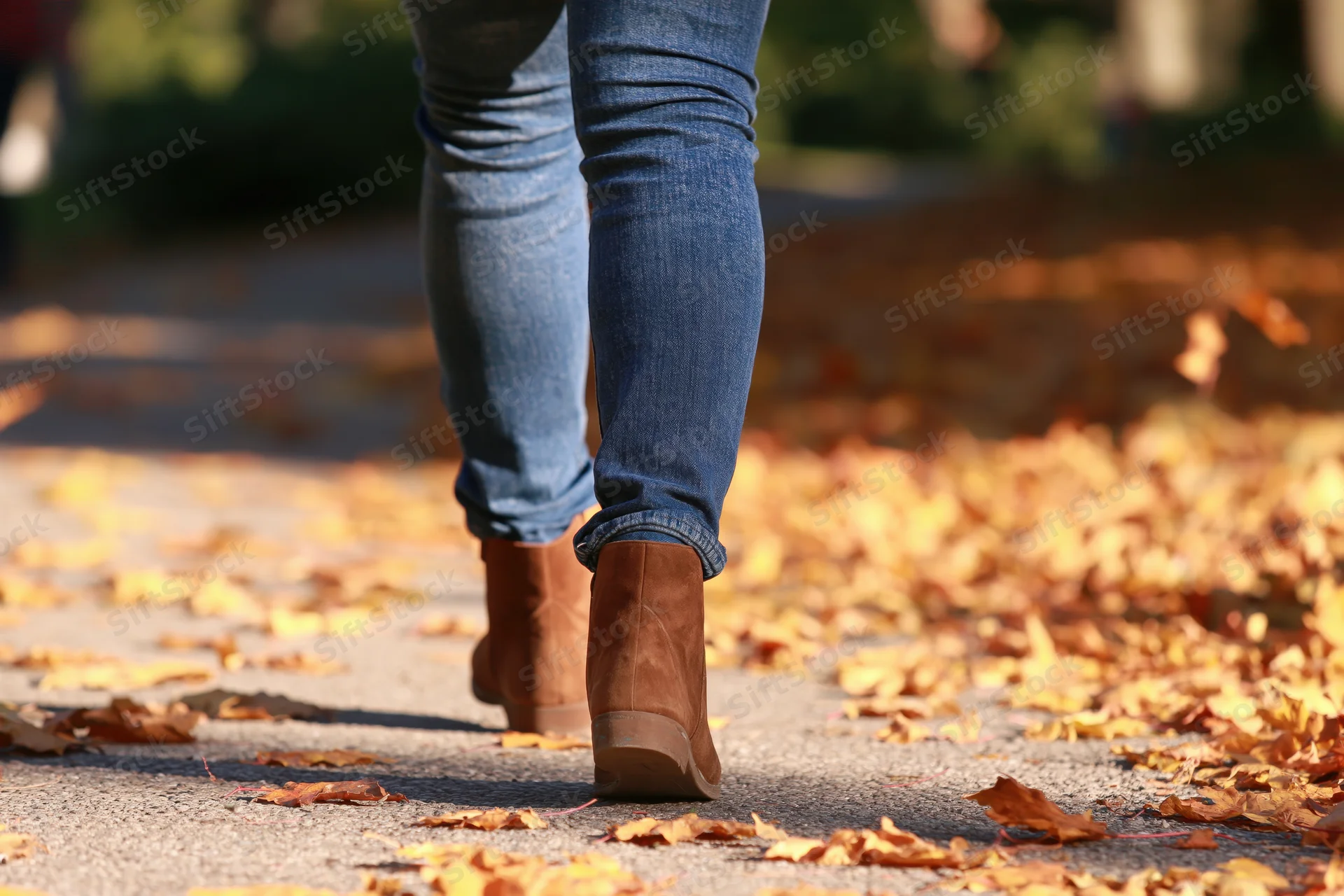 Woman walking away on a leaf-covered sidewalk in autumn