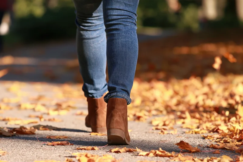 Woman walking away on a leaf-covered sidewalk in autumn