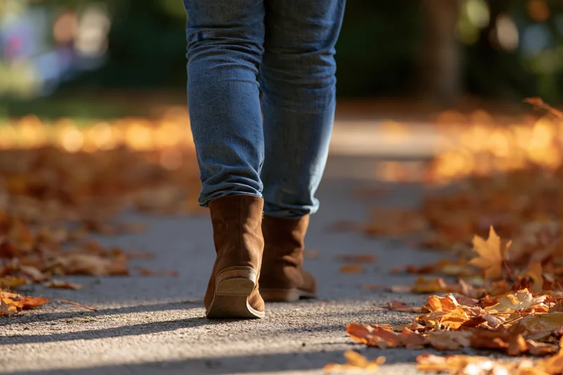 Woman walking away on a leaf-covered sidewalk in autumn