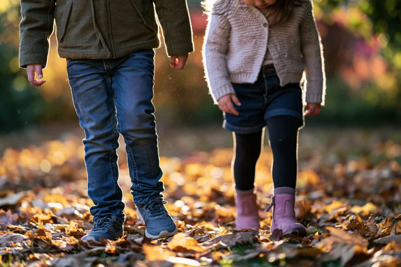 Two children walking through fallen autumn leaves in a yard