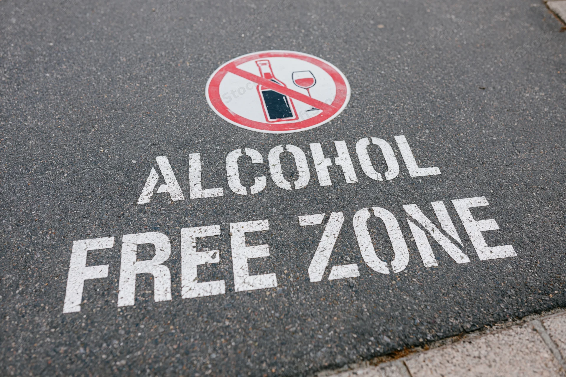 Alcohol free zone text stenciled on dark asphalt pavement