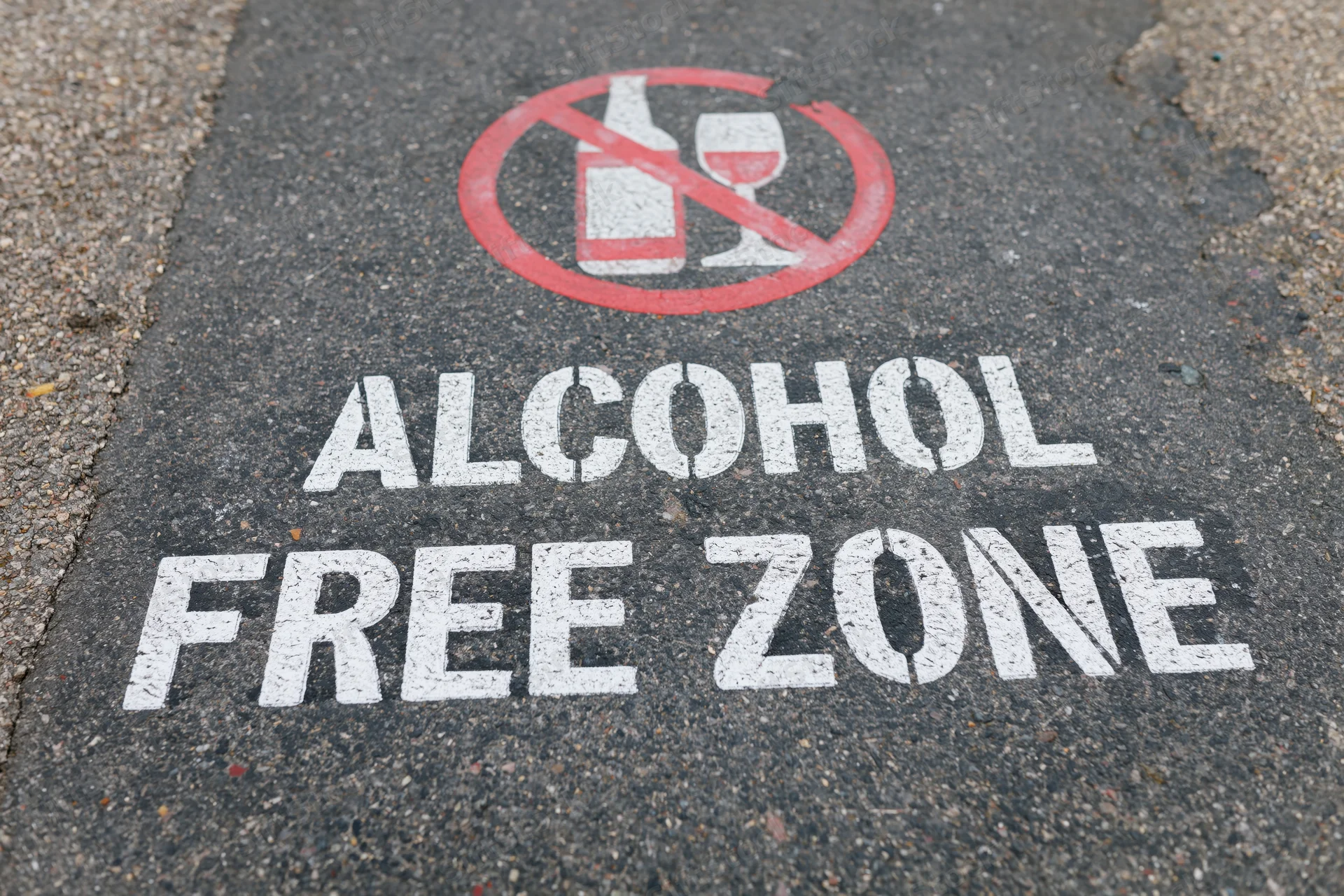 Alcohol free zone sign stenciled in white and red paint on dark asphalt pavement