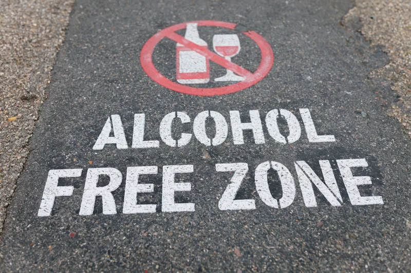 Alcohol free zone sign stenciled in white and red paint on dark asphalt pavement