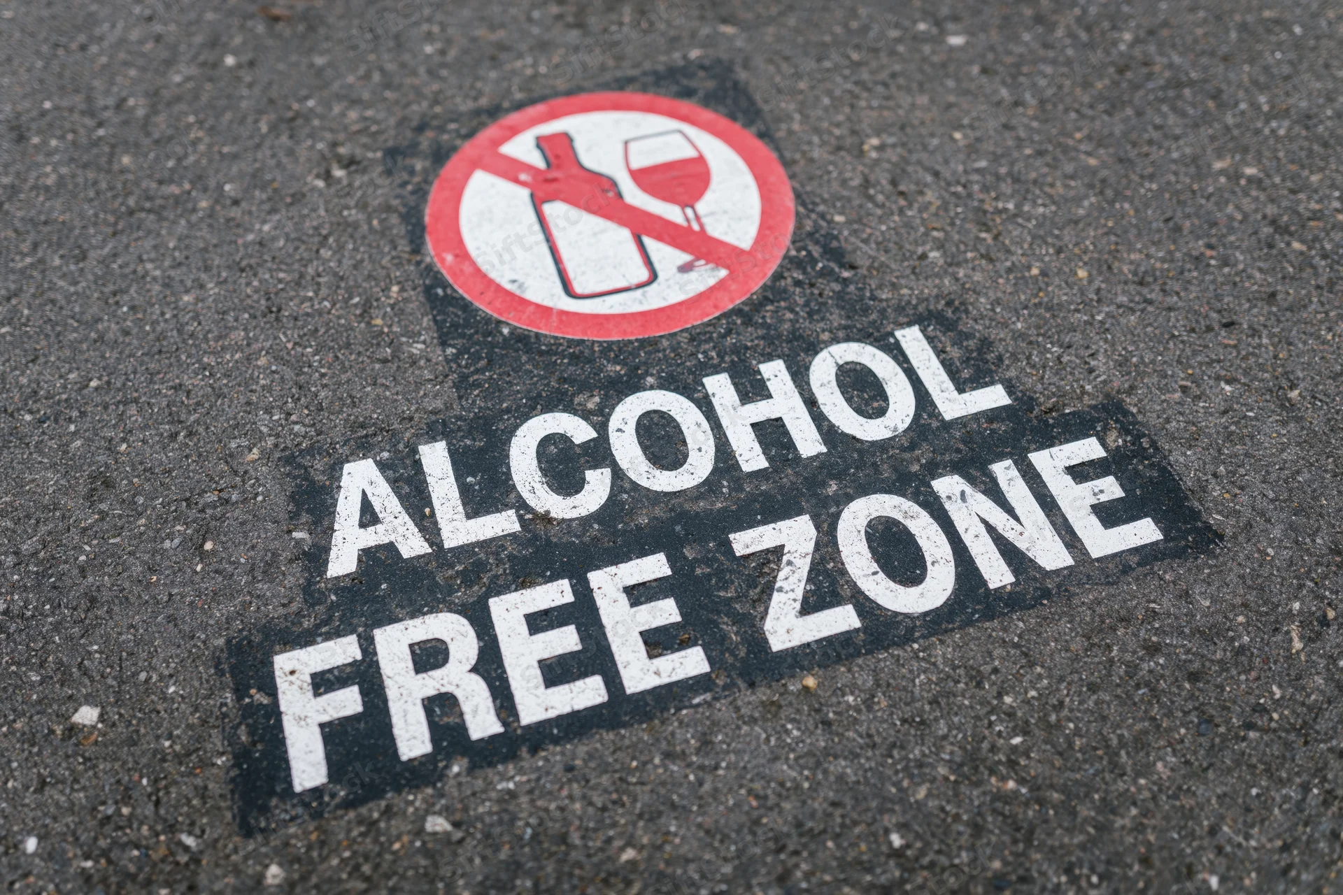 Alcohol free zone text stenciled on dark asphalt pavement