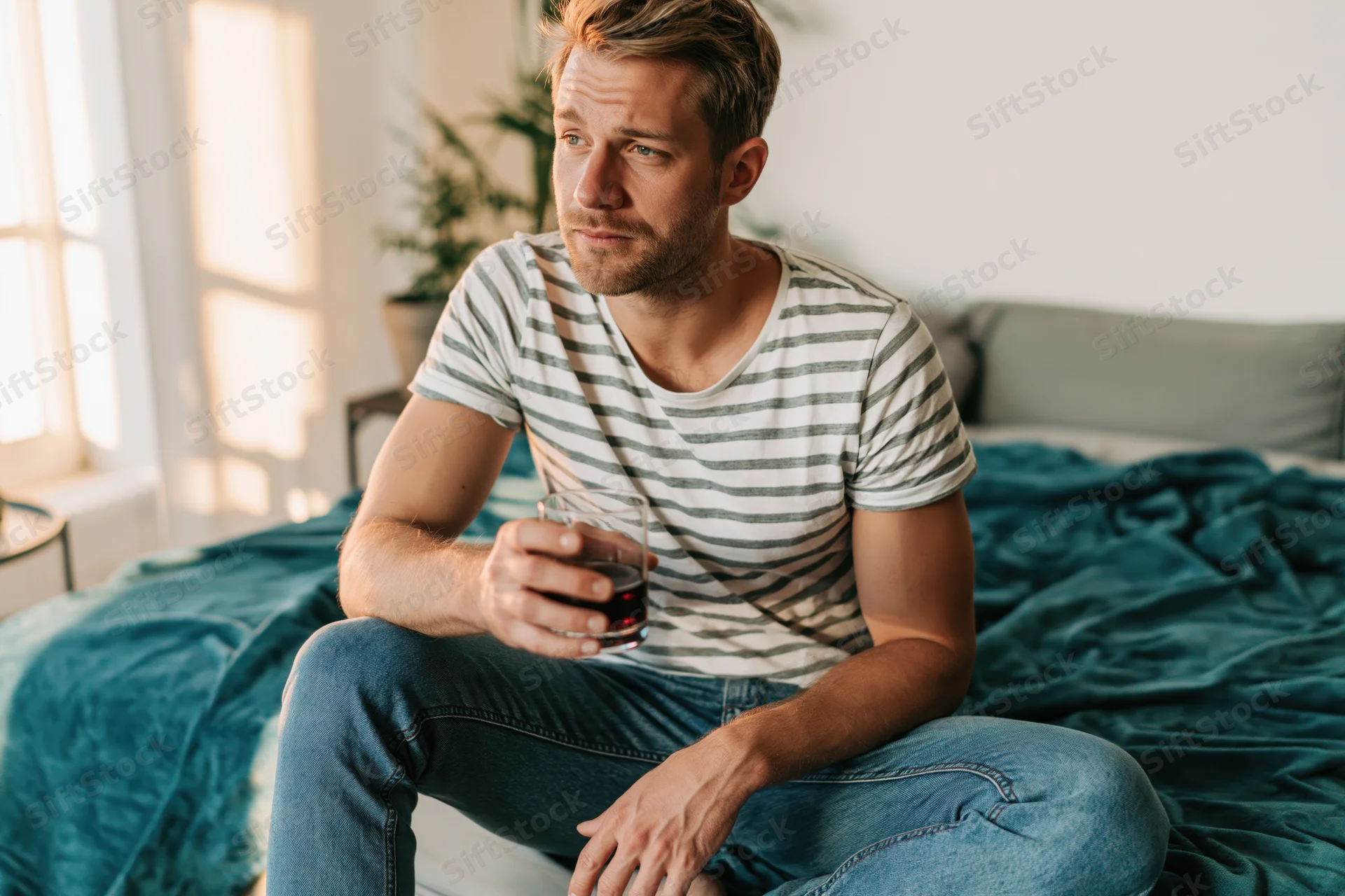 Man sitting on bed holding glass of red wine in bedroom