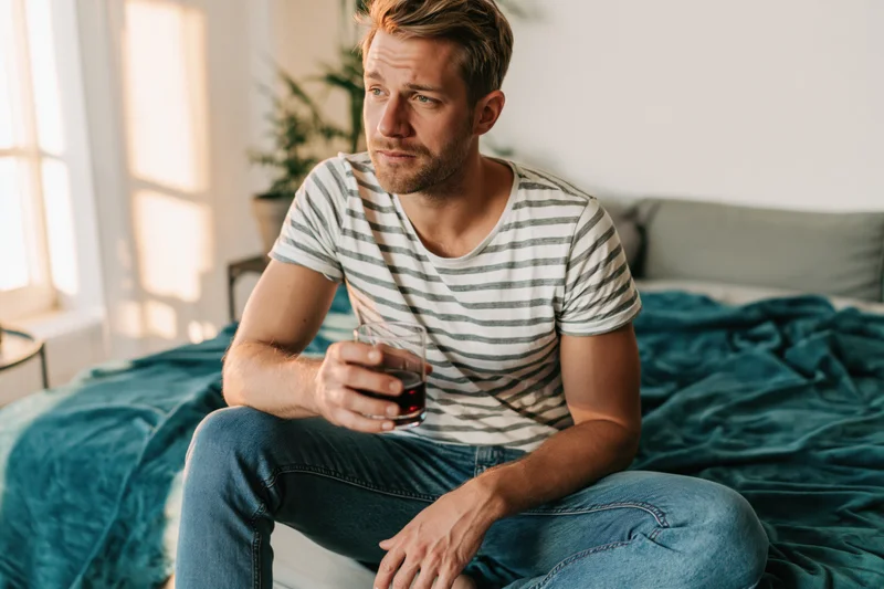 Man sitting on bed holding glass of red wine in bedroom