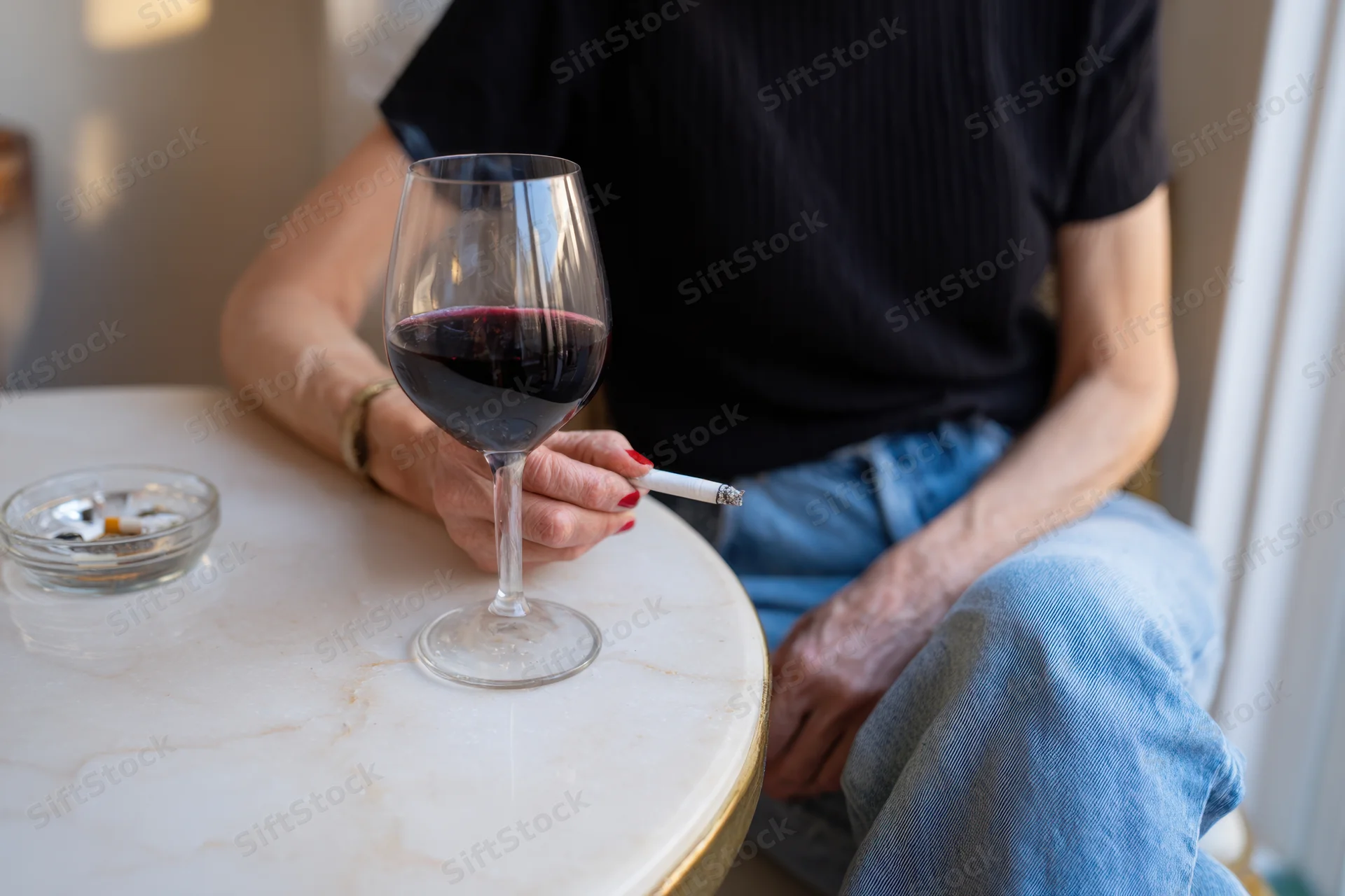 Woman seated at marble table holding cigarette with glass of red wine beside her