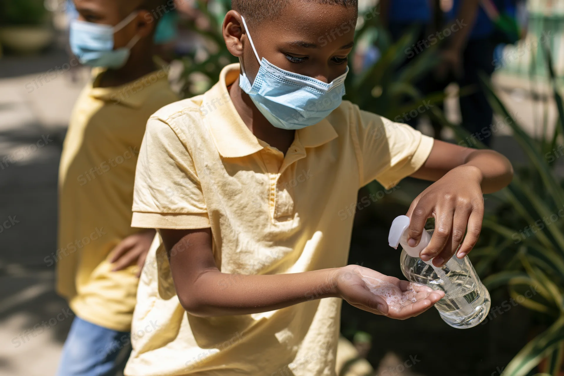Young boy wearing a mask and dispensing hand sanitizer outdoors in a garden setting