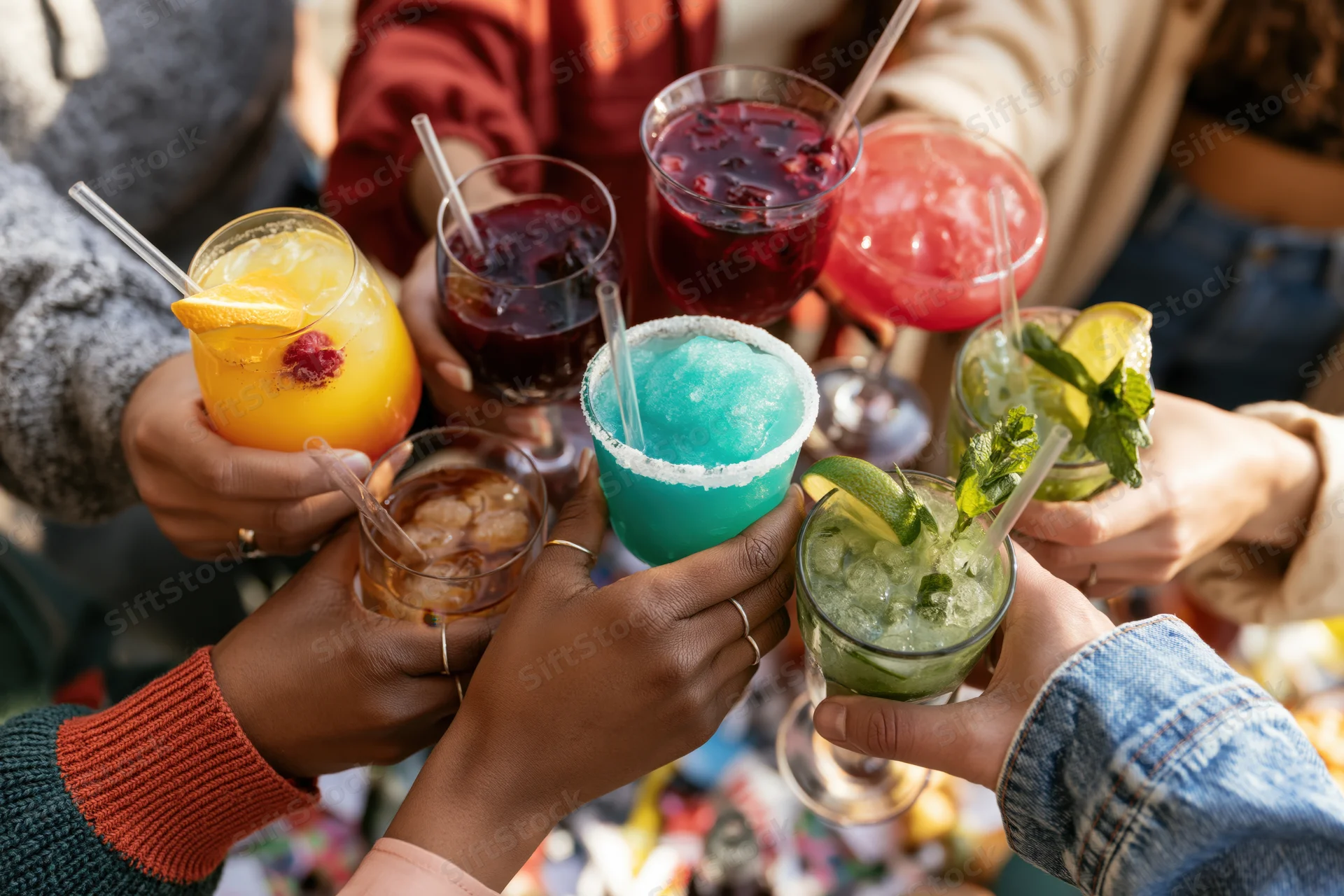 Diverse group toasting with colorful cocktails at a summer outdoor party
