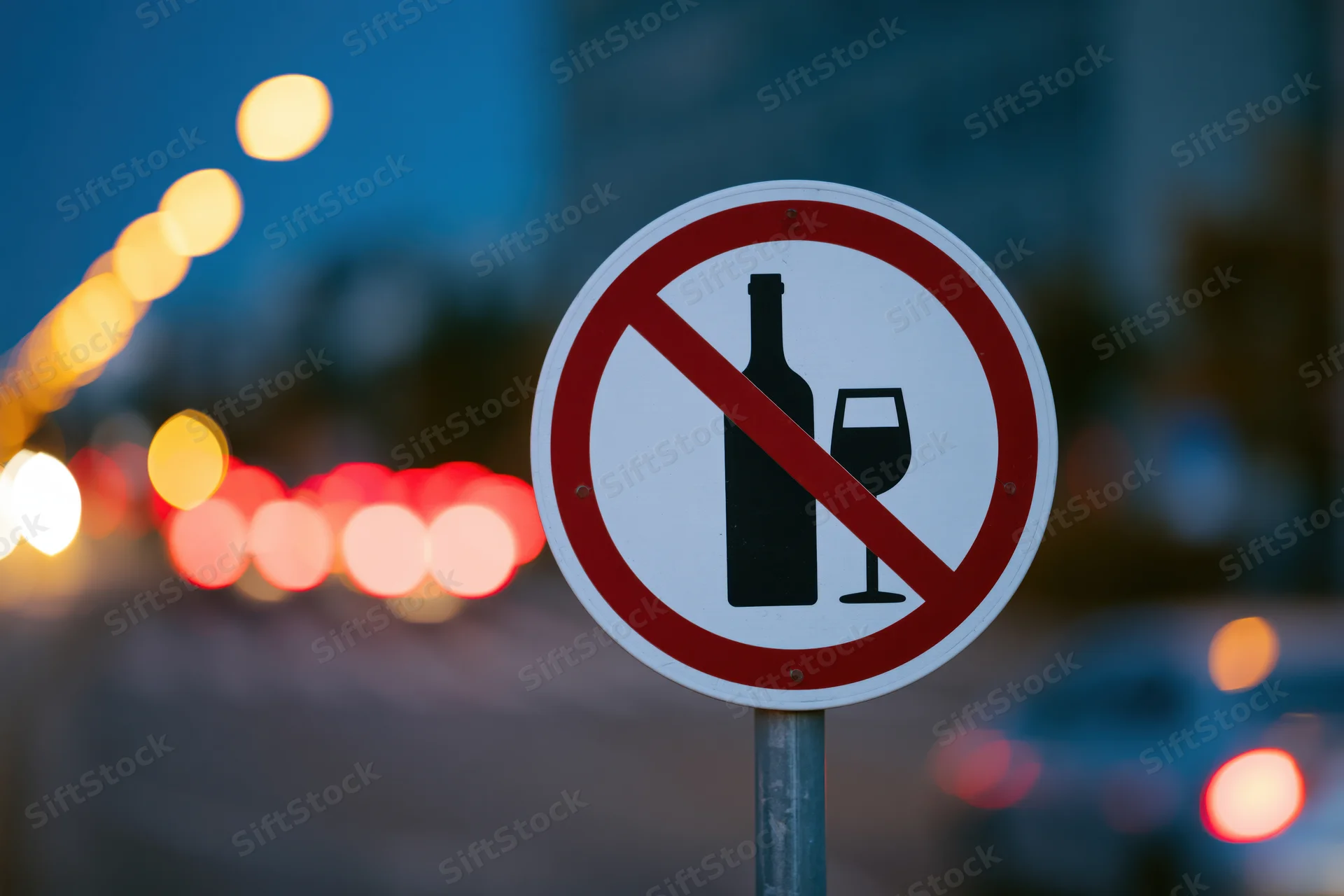 Circular no-alcohol prohibition sign on metal pole by city street at twilight
