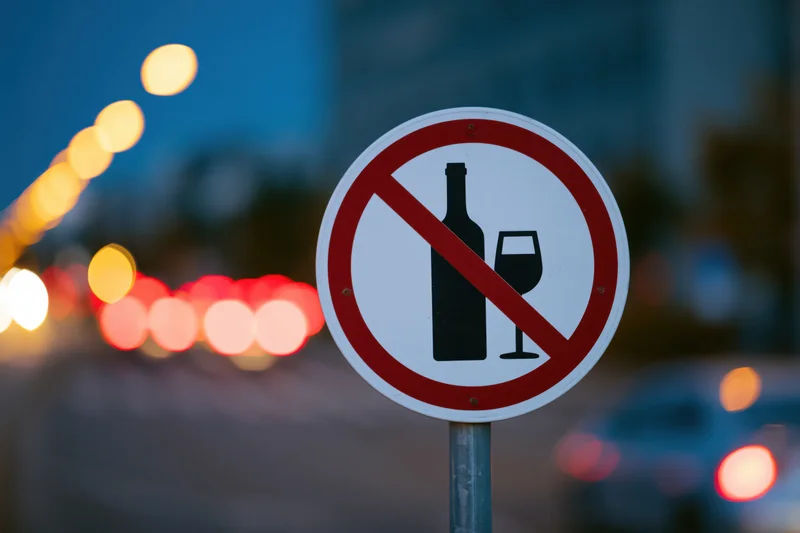 Circular no-alcohol prohibition sign on metal pole by city street at twilight