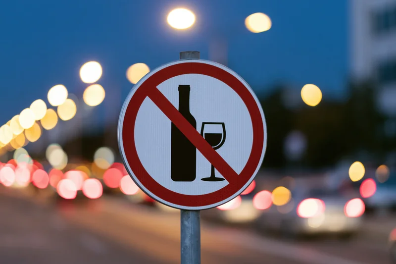 Circular no-alcohol prohibition sign on metal pole by city street at twilight