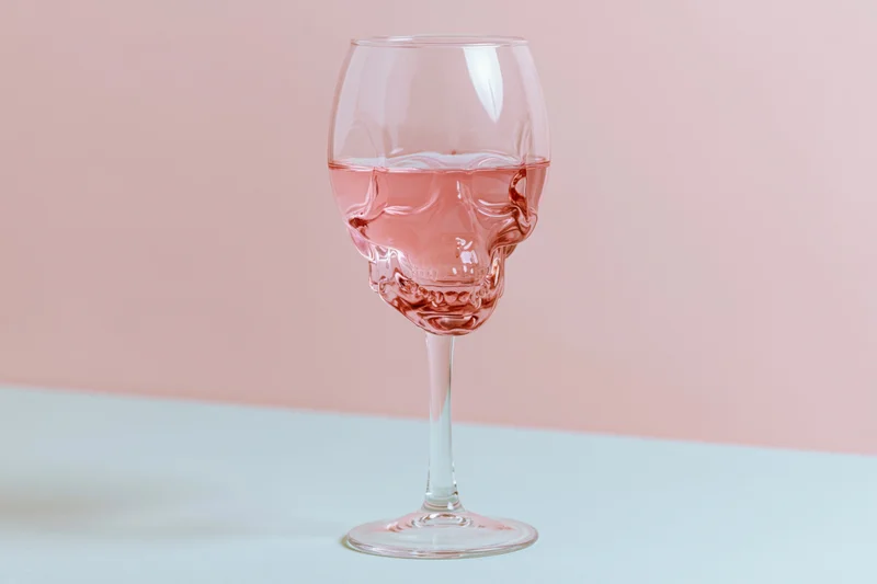Skull-shaped wineglass filled halfway with pink liquid on a pastel surface