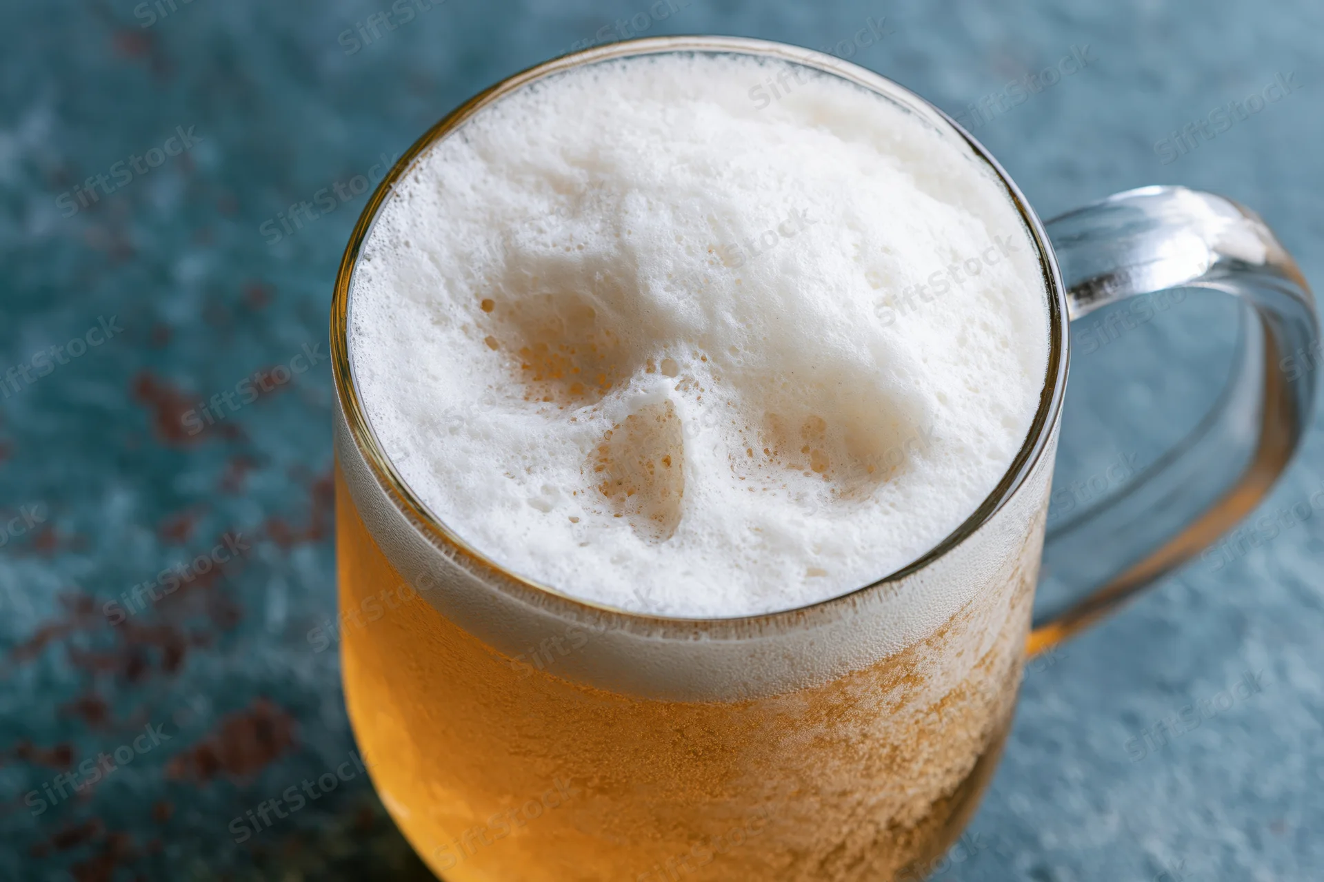 Golden lager in a glass mug with thick white foam on a textured blue surface