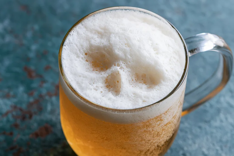 Golden lager in a glass mug with thick white foam on a textured blue surface
