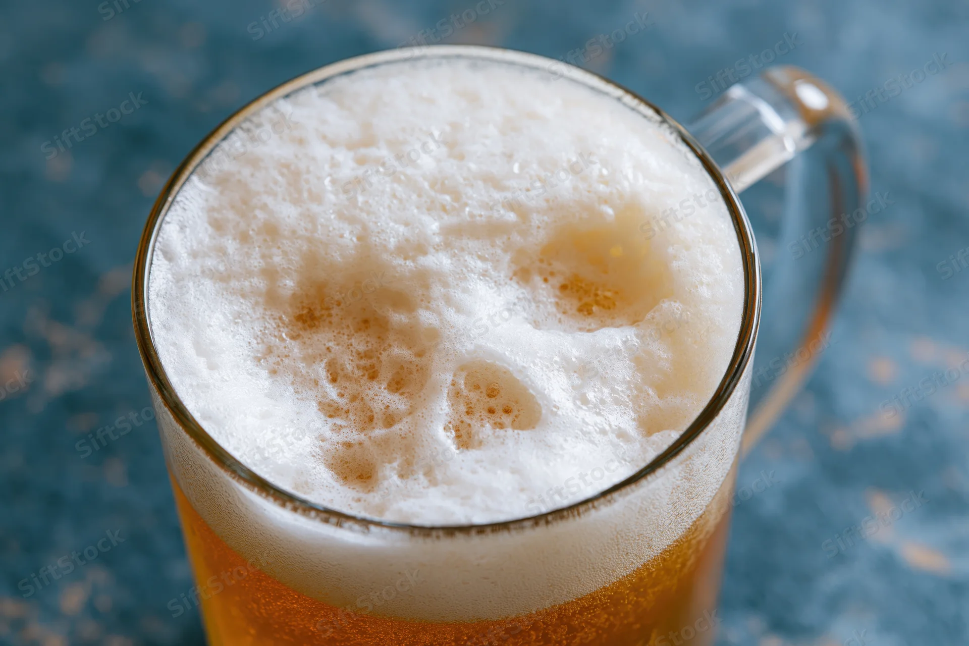 Glass beer mug filled with golden lager and thick white foam on blue surface