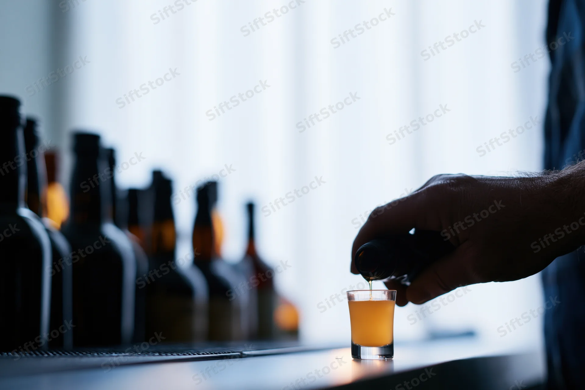 Bartender pouring amber liquid into a shot glass at a dimly lit bar counter