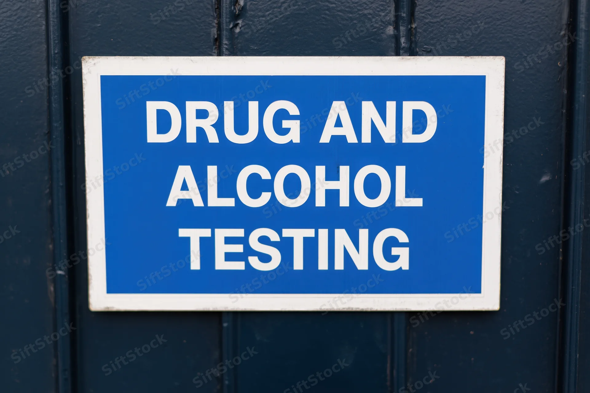 Blue rectangular sign reading drug and alcohol testing mounted on dark door