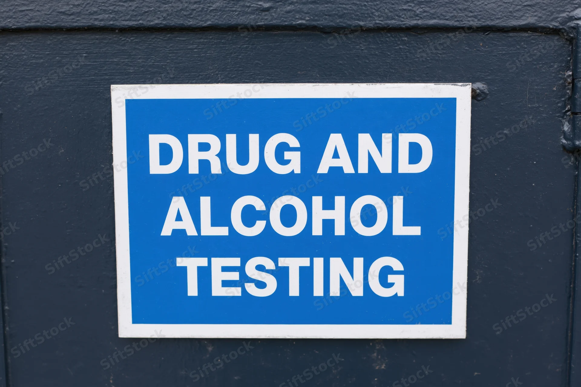 Blue sign reading drug and alcohol testing mounted on dark door