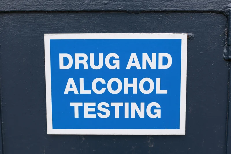 Blue sign reading drug and alcohol testing mounted on dark door