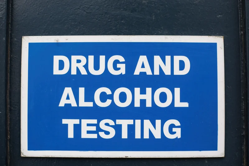 Blue sign with white text reading drug and alcohol testing mounted on dark surface