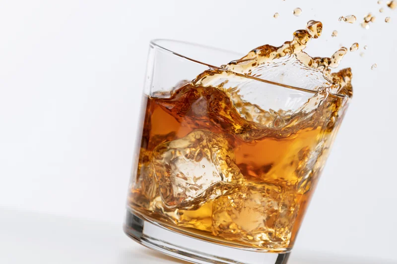 Amber whiskey splashing in a rocks glass with ice cubes on white background