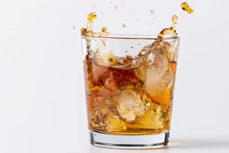 Amber whiskey splashing in a rocks glass with ice cubes on white background