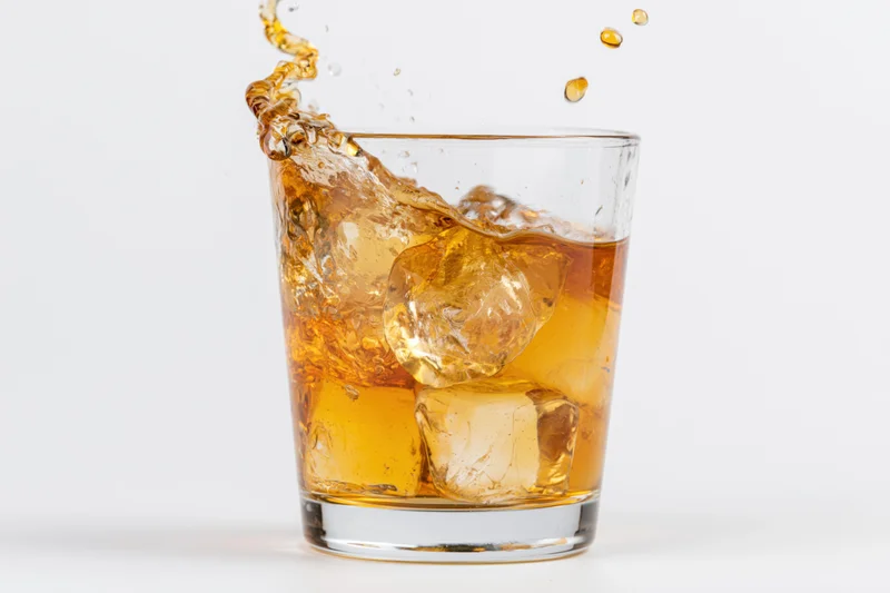 Amber whiskey splashing in a rocks glass with ice cubes on white background