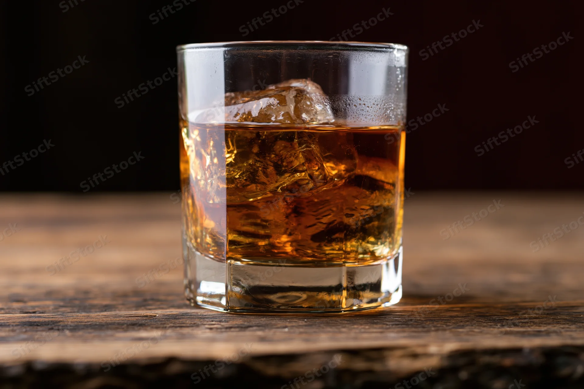 Amber whiskey with ice in a rocks glass on a wooden table