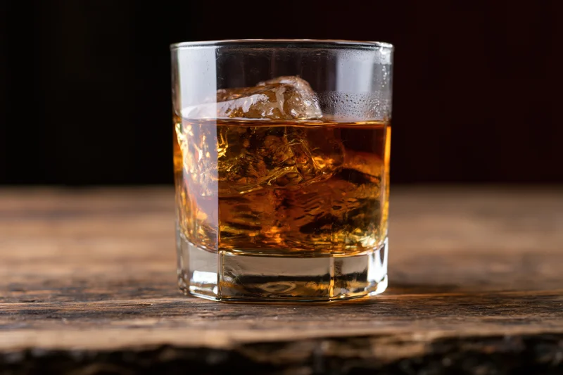 Amber whiskey with ice in a rocks glass on a wooden table