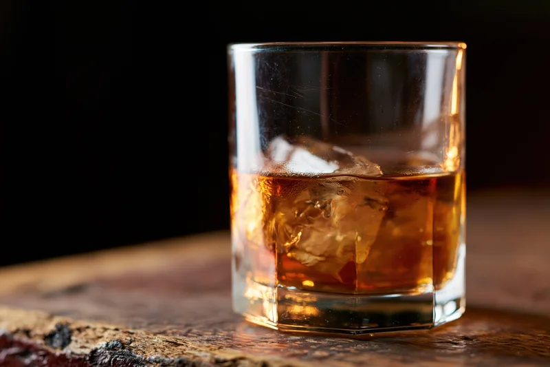 Amber whiskey with ice in a rocks glass on a wooden table