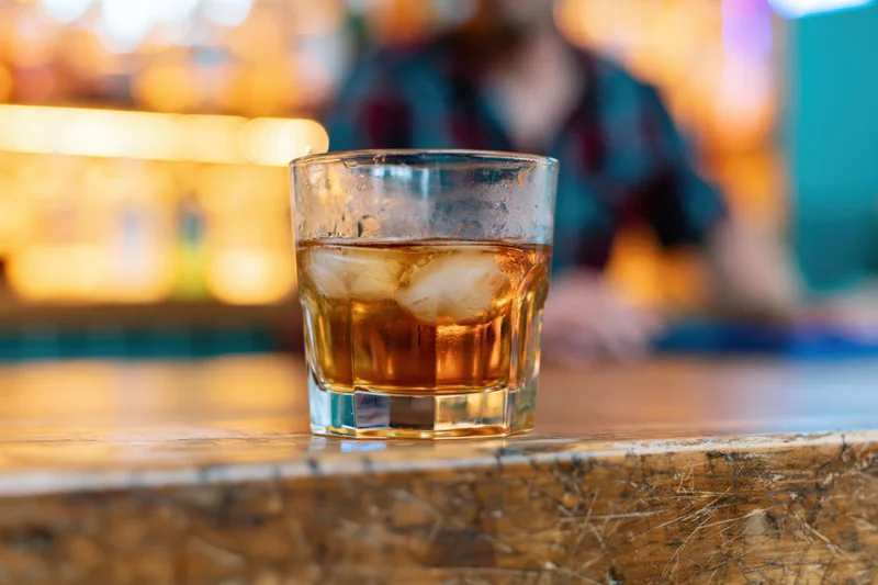 Amber whiskey with ice in a rocks glass on a wooden bar counter