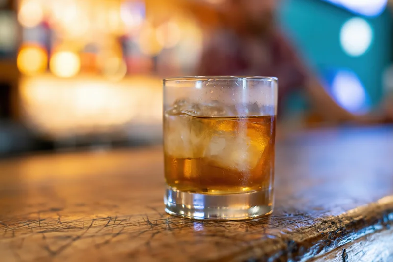 Amber whiskey with ice in a rocks glass on a wooden bar top