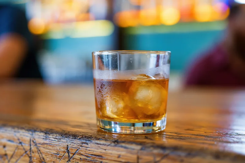 Amber whiskey with ice in a rocks glass on a wooden bar table
