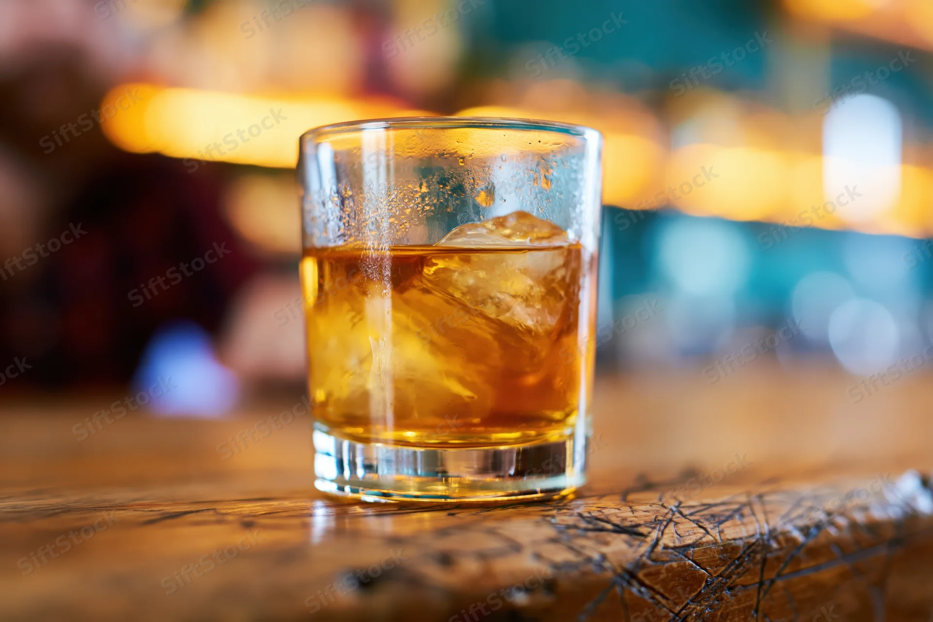 Amber whiskey with ice in a rocks glass on a wooden bar surface