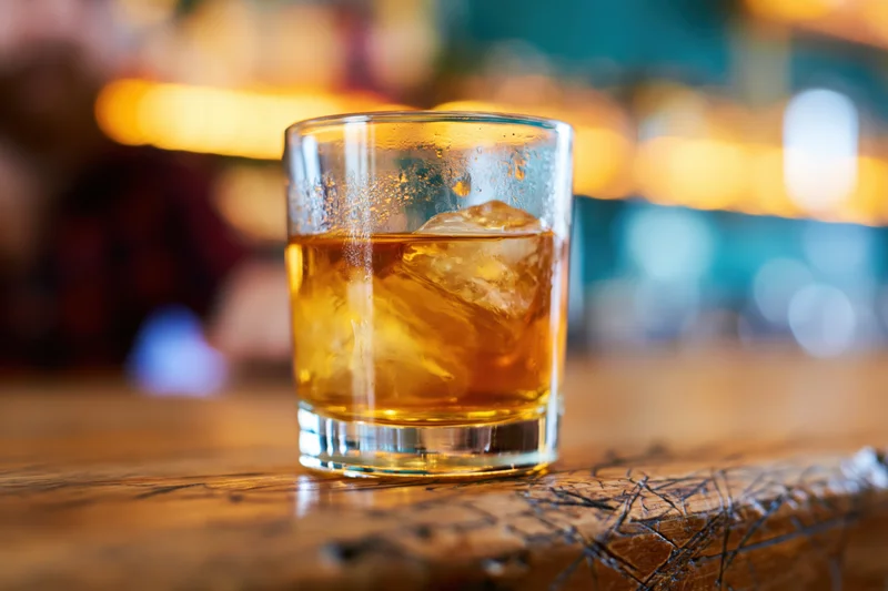 Amber whiskey with ice in a rocks glass on a wooden bar surface