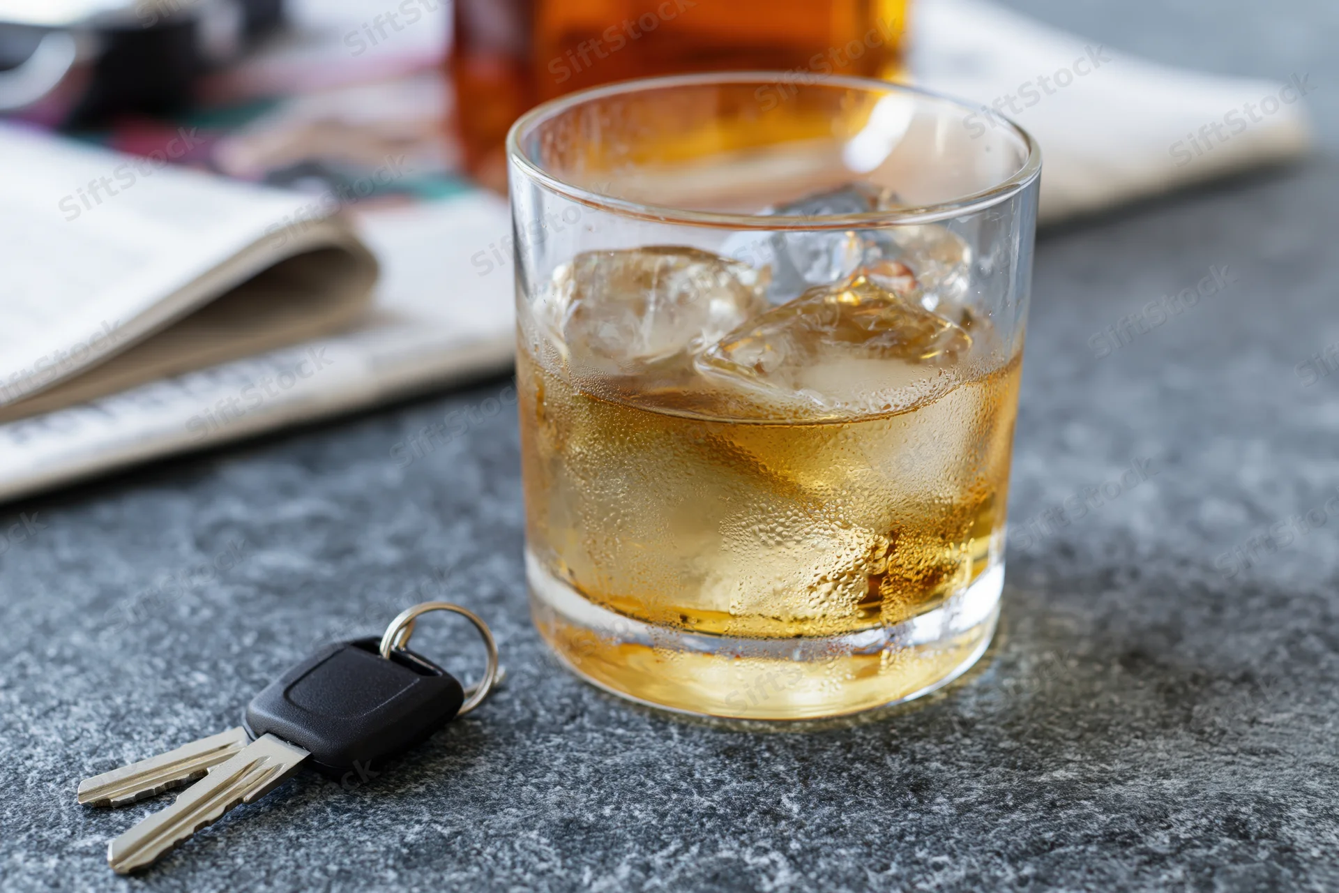 Whiskey in a rocks glass with ice and car keys on a dark countertop