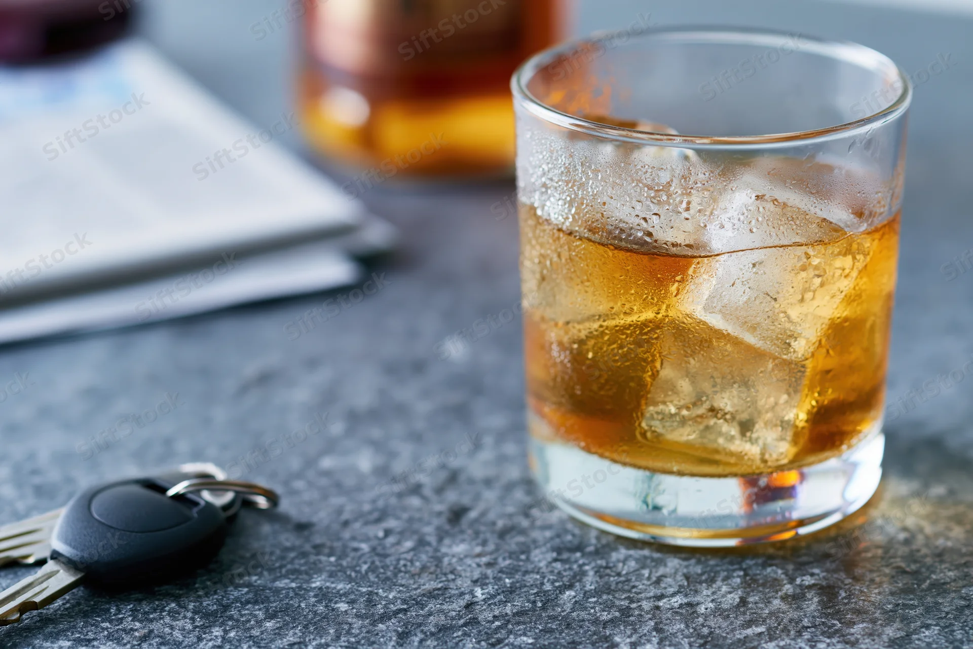 Whiskey in a rocks glass with ice and car keys on a dark countertop
